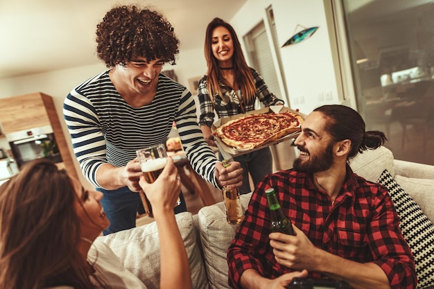 Glückliche Freunde, die Spaß haben, während sie Pizza essen und Bier trinken. Sie haben ein tolles Wochenende in netter Gesellschaft drinnen.