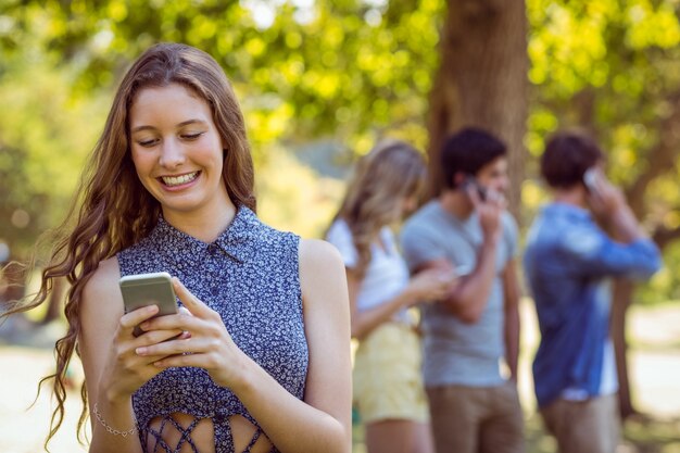 Glückliche Freunde im Park unter Verwendung ihrer Telefone