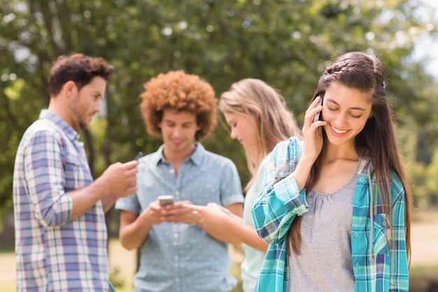 Glückliche Freunde im Park unter Verwendung ihrer Telefone