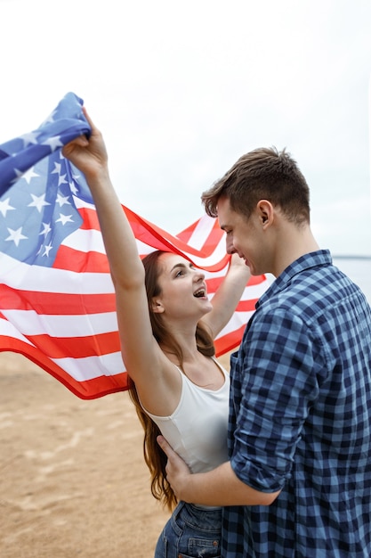 Glückliche Freunde verbringen Zeit am Strand und halten die amerikanische Flagge