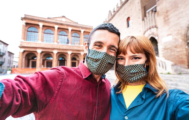 Glückliche Freundin und verliebter Freund, die Selfie nehmen, das durch Gesichtsmaske bei Altstadttour bedeckt wird