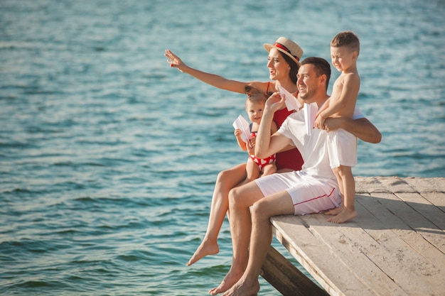 Glückliche fröhliche Familie am Pier nahe dem Wasser, das Spaß hat. Entzückende Kinder, die mit ihren Eltern spielen