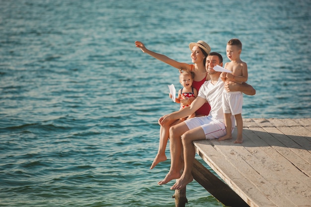 Glückliche fröhliche Familie am Pier nahe dem Wasser, das Spaß hat. Entzückende Kinder, die mit ihren Eltern spielen