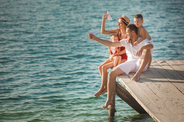 Glückliche fröhliche Familie am Pier nahe dem Wasser, das Spaß hat. Entzückende Kinder, die mit ihren Eltern spielen