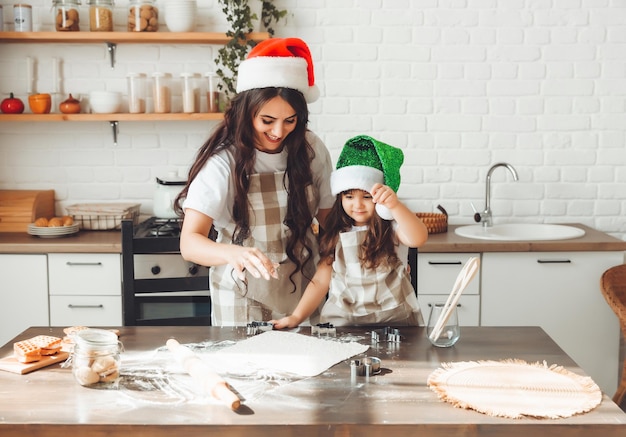 Glückliche, fröhliche Mutter und Kind in Weihnachtsmannmützen kochen Weihnachtsplätzchen in der Küche, Neujahr und Weihnachten
