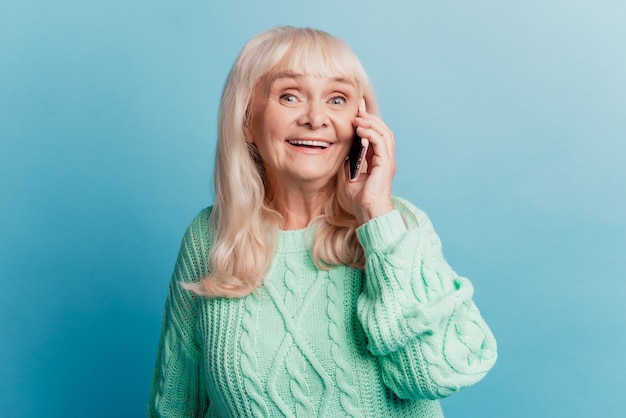 Glückliche fröhliche reife Frau, die auf dem Smartphone spricht, das auf blauem Hintergrund lokalisiert wird