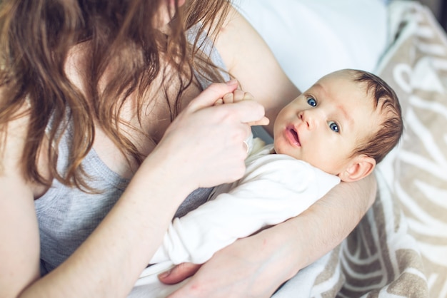 Glückliche fürsorgliche Mutter, die einen lächelnden Jungen im Schlafzimmer hält