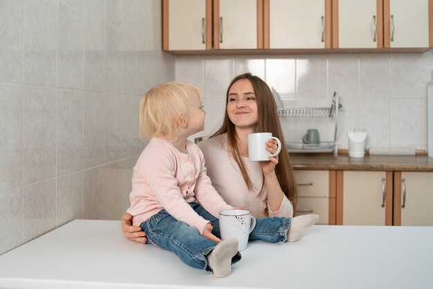 Glückliche fürsorgliche Mutter und kleines blondes Mädchen frühstücken in der Küche.