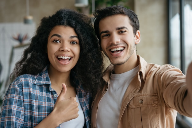 Glückliche gemischte Rassenfreunde, die Selfies auf Handy nehmen und im modernen Café lachen