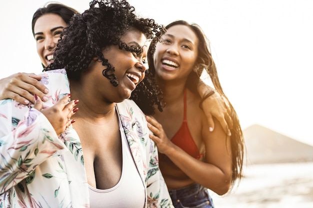 Glückliche gemischtrassige Frauen mit unterschiedlichen Körpern und Haut, die sich am Sommertag am Strand amüsieren - Fokus auf afrikanischem Mädchengesicht