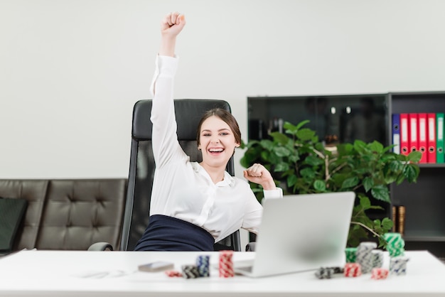 Glückliche Geschäftsfrau gewinnt im on-line-Kasino beim Spielen des Pokers im Büro am Arbeitsplatz