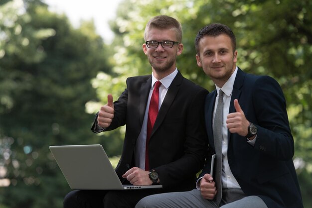 Glückliche Geschäftsleute mit Tablet-PC draußen auf einer Parkbank