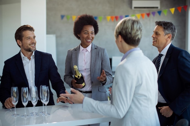 Glückliche Geschäftsleute unterhalten sich, während sie ihren Erfolg mit Champagner im Büro feiern