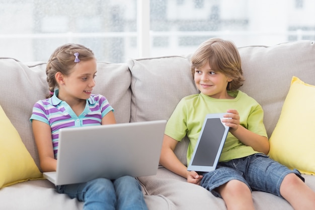 Foto glückliche geschwister, die technologien auf sofa verwenden