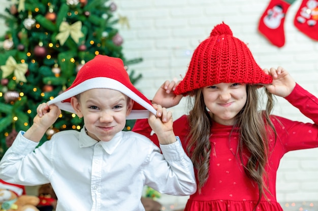 Glückliche Geschwister in Weihnachtsoutfits auf dem Boden nahe dem Weihnachtsbaum zu Hause. Glückliche Familienidee