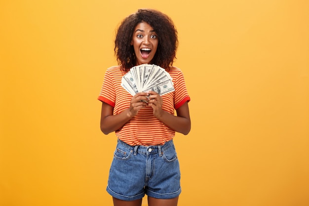 glückliche glückliche junge afroamerikanische junge Frau mit dem lockigen Haar, das Bündel Geld hält und vor Freude schreit