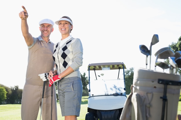 Glückliche Golf spielende Paare, die hinten mit Golfbuggy zeigen