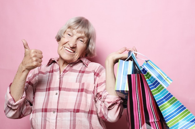 Glückliche Großmutter mit Einkaufstaschen über rosa Hintergrund. Lifestyle und People-Konzept.