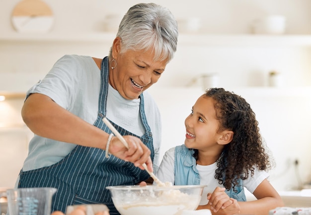 Glückliche Großmutter oder Kind, das als glückliche Familie in der Küche backt, während ein junges Mädchen das Rezept für Kekse lernt, die Entwicklung von Kuchen mischt, oder lächelnde Großmutter oder Kind, das dem Kind beibringt, mit Eiern, Butter oder Mehl zu backen