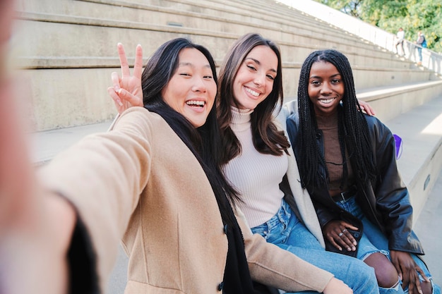 Glückliche Gruppe gemischtrassiger junger Frauen, die ein Selfie-Porträt machen, das in die Kamera lächelt Drei verschiedene Mädchen, die Spaß im Freien haben Beste Freunde, die ein Foto machen