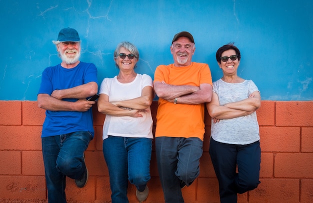 Glückliche Gruppe von vier älteren Leuten in Freundschaft, die gegen eine orange und blaue Wand steht und lächelt und in die Kamera schaut. Fröhliche und lustige Gesichter.