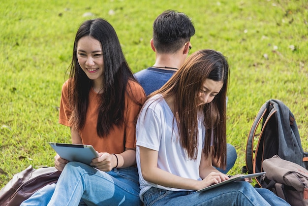 Glückliche Gruppenfreunde Studenten sitzen im Park an der Universität und lesen zusammen Laptop und Tablet