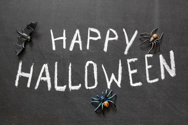 Glückliche Halloween-Nachricht handgeschrieben auf Tafel mit Spinnen herum
