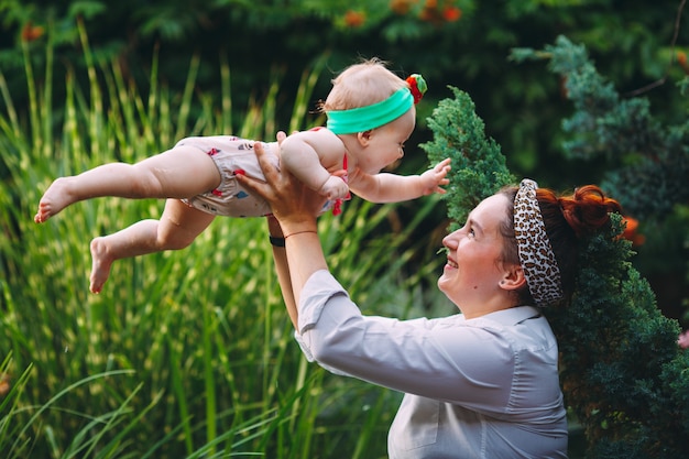 Glückliche harmonische Familie draußen. Mutter wirft Baby auf, lacht und spielt im Sommer