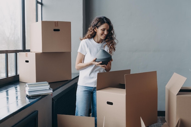 Glückliche Hausbesitzerin packt am Umzugstag eine Kiste mit Habseligkeiten im neuen Zuhause aus Hypothekenwerbung