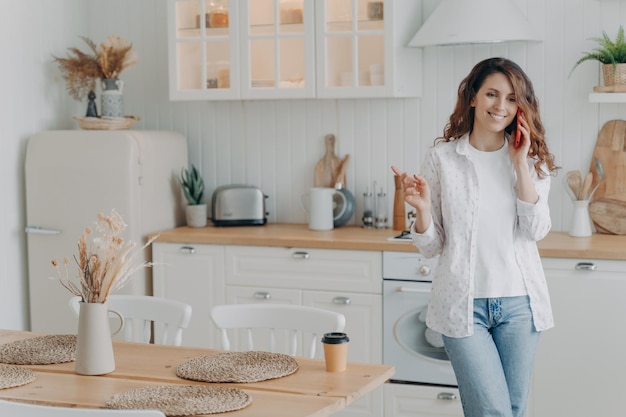 Glückliche Hausfrau hat Freizeit und spricht auf dem Smartphone in der Küche Modernes skandinavisches Interieur