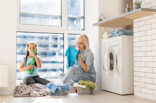 Glückliche Hausfrau und ihre Tochter mit Bettwäsche in der Nähe der Waschmaschine