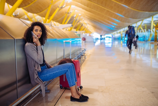 Glückliche hörende Musik der jungen Frau mit Kopfhörern und Handy am Flughafen