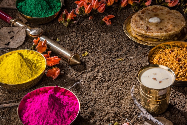 Glückliche Holi-Grußkarte, die indisches traditionelles süßes und salziges Essen, Blumen und Pulverfarben zeigt, die über weißem Hintergrund oder Ton angeordnet sind. Selektiver Fokus