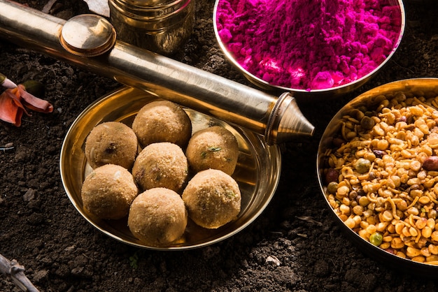Glückliche Holi-Grußkarte, die indisches traditionelles süßes und salziges Essen, Blumen und Pulverfarben zeigt, die über weißem Hintergrund oder Ton angeordnet sind. Selektiver Fokus