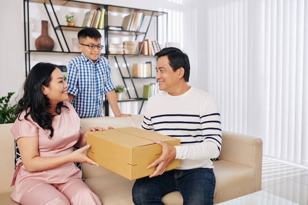 Glückliche hübsche asiatische Frau, die Geburtstagsgeschenk von Ehemann und Sohn empfängt
