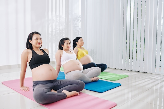 Glückliche hübsche junge vietnamesische schwangere Frauen, die im Trainingskurs auf Yogamatten sitzen