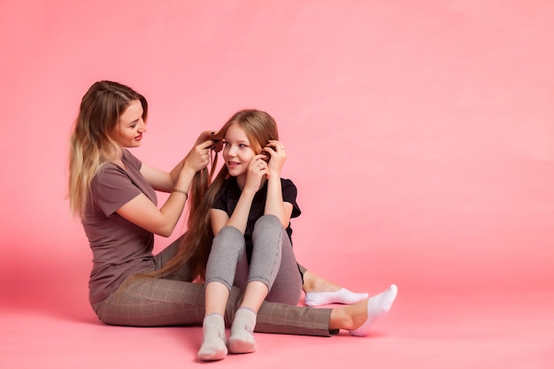 Glückliche hübsche Mutter und ihre kleine Tochter, die ihr Haar auf rosafarbenem Hintergrund sanft kämmt