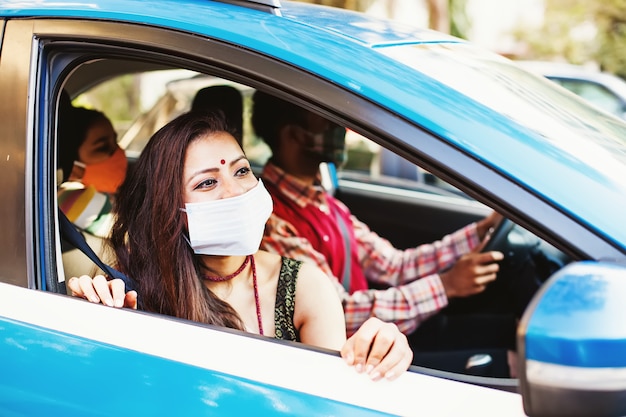 Glückliche indische Familie mit Coronavirus-Schutzmasken, die zusammen in einem Auto reisen car