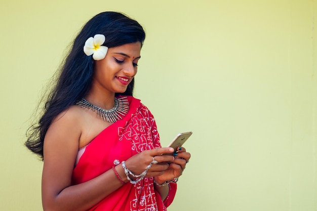 Glückliche indische geschäftsdame weißes zahniges lächeln in traditioneller indischer sari-kleidung rotes hochzeitskleid mit einem gerät in der hand mit der telefon-app in der tropischen insel felsen urlaub indian bay.girl gesicht id