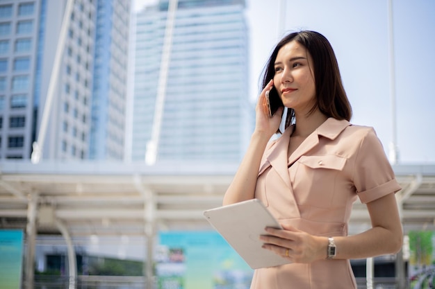 Glückliche intelligente Geschäftsfrau, die ein intelligentes Telefon in der Stadt verwendet