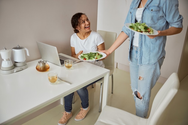 Glückliche internationale Frau, die Teller mit Salat nimmt