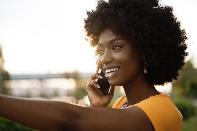 Glückliche junge afrikanisch-amerikanische junge Frau, die mit dem Handy in der Stadt spricht