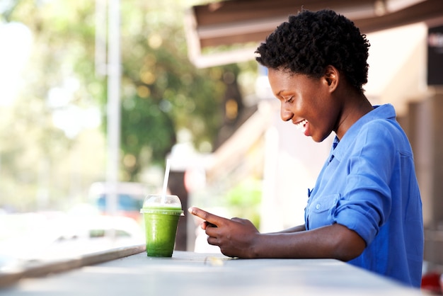 Glückliche junge afrikanische Frau, die am Café unter Verwendung des Handys sitzt