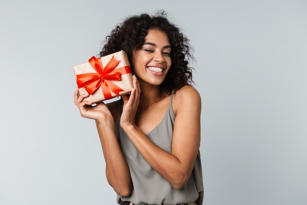 Glückliche junge afrikanische Frau lässig gekleidet stehend isoliert, eine Geschenkbox haltend