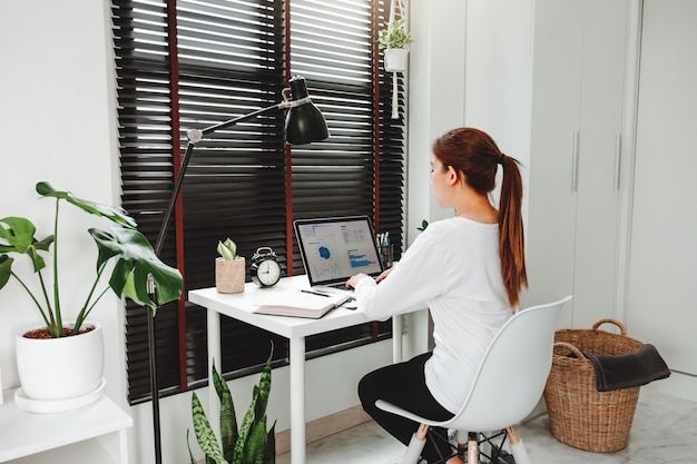 Glückliche junge asiatische Frau arbeiten von zu Hause aus und arbeiten an einem sozialen Laptop-Netzwerk