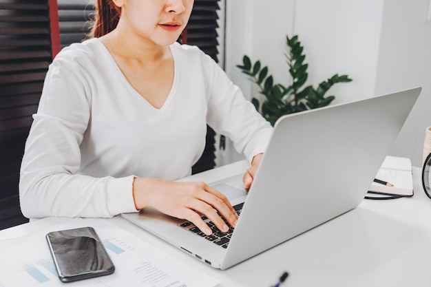 Glückliche junge asiatische Frau arbeiten von zu Hause aus und arbeiten an einem sozialen Laptop-Netzwerk