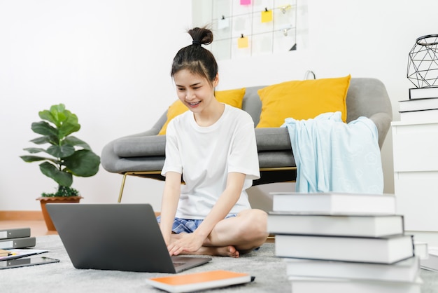 Glückliche junge asiatische Frau, die für Laptop mit Grafikdokumenten von zu Hause auf dem Teppich, Treffen und Training Online-Konzept arbeitet.