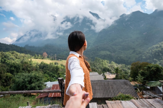 Glückliche junge asiatische Frau, die Händchen ihres Freundes hält, während sie den Bergblick auf dem Hügel am Aussichtspunkt in Chiang Dao, Thailand genießt