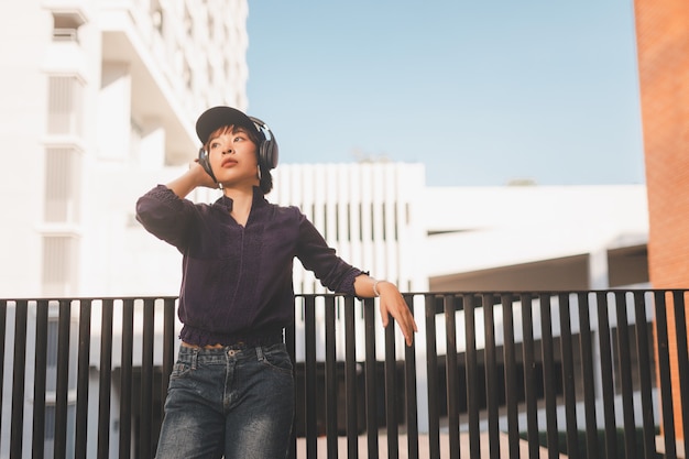 Glückliche junge asiatische Frau, die Musik hört und Spaß mit Kopfhörern auf der Straße hat.