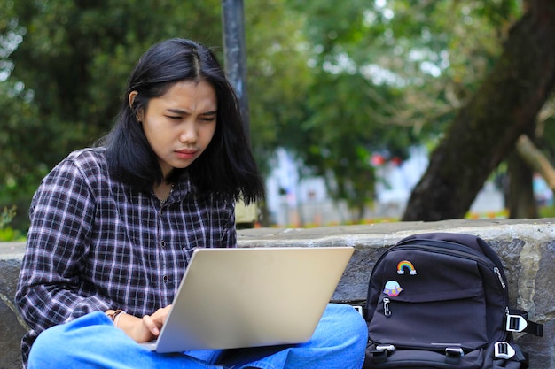 glückliche junge asiatische Frau, die sich auf den Laptop konzentriert, arbeitet aus der Ferne und surft in sozialen Medien im Freien